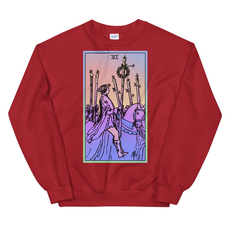 May include: Red sweatshirt with a graphic of the Six of Wands tarot card. The card features a rider on horseback with a crown of laurels and a staff. The card is surrounded by a blue and green border.