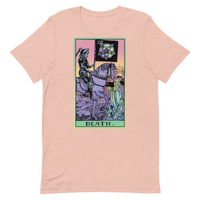 Puede incluir: Camiseta rosa claro con un dise&ntilde;o de carta del tarot. El gr&aacute;fico representa una figura esquel&eacute;tica a caballo, sosteniendo una bandera con una rosa. La palabra "DEATH" est&aacute; impresa en la parte inferior del dise&ntilde;o.