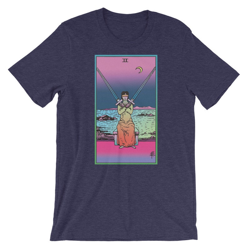 Op de afbeelding: Een marineblauw t-shirt met een kleurrijke illustratie van de tarotkaart Twee van Zwaarden. De kaart toont een figuur met een blinddoek die twee zwaarden gekruist over zijn borst vasthoudt.