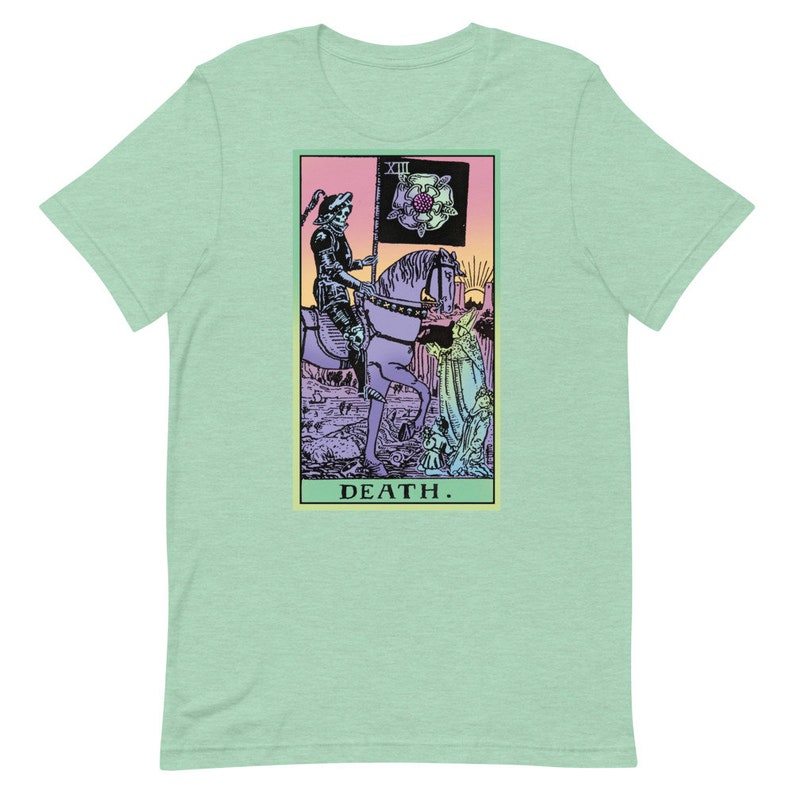 Puede incluir: Una camiseta verde claro con un dise&ntilde;o de carta del tarot. El gr&aacute;fico representa una figura esquel&eacute;tica a caballo, sosteniendo una bandera con una rosa. La palabra "DEATH" est&aacute; impresa en la parte inferior de la carta.