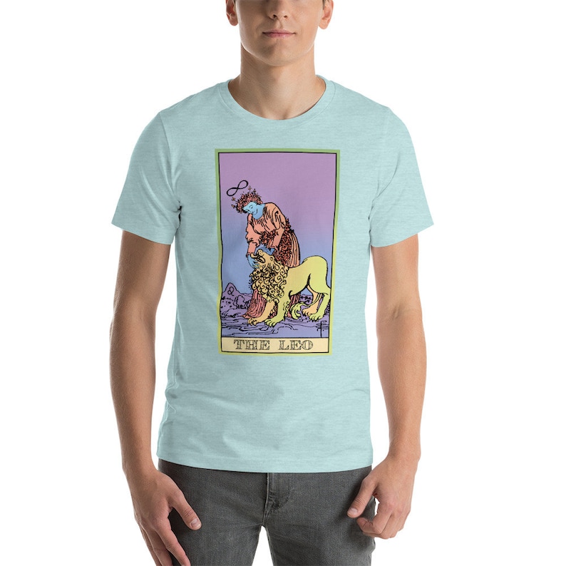 May include: A light blue t-shirt with a graphic of a tarot card, The Leo. The card features a woman with a halo and a lion. The card is in a pastel color scheme with a purple, pink, and yellow gradient.