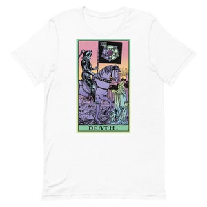 Puede incluir: Camiseta blanca con un dise&ntilde;o de carta del tarot. El gr&aacute;fico muestra una figura esquel&eacute;tica a caballo sosteniendo una bandera con una rosa. La palabra "DEATH" est&aacute; impresa en la parte inferior. El dise&ntilde;o tiene una paleta de colores pastel.