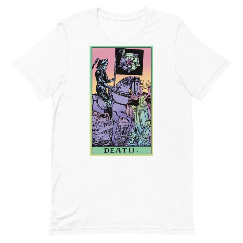 Puede incluir: Camiseta blanca con un dise&ntilde;o de carta del tarot. El gr&aacute;fico muestra una figura esquel&eacute;tica a caballo sosteniendo una bandera con una rosa. La palabra "DEATH" est&aacute; impresa en la parte inferior. El dise&ntilde;o tiene una paleta de colores pastel.