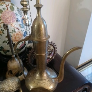 May include: A brass teapot with a decorative handle and a spout. The teapot has a round body and a tall, slender neck. The teapot is decorated with intricate engravings.