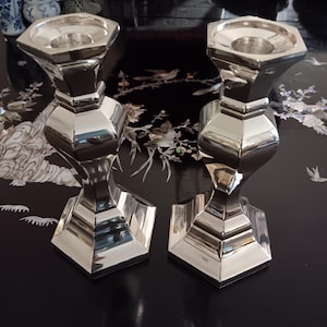 May include: Two silver candle holders with a geometric design. The candle holders are on a black surface with a floral pattern.