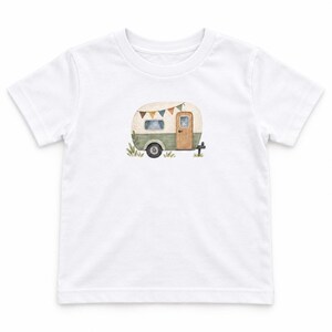 May include: A white short-sleeve t-shirt featuring a centered watercolor illustration of a vintage-style camper trailer. The camper is cream and sage green with a wooden door, a single wheel, and a string of colorful triangular bunting flags.