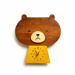 May include: A wooden bear-shaped clock with a yellow face and black numbers. The clock hands are gold.