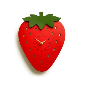 May include: A red wooden wall clock shaped like a strawberry, with a green leaf and stem. The clock face has black numbers and gold-coloured hands. The clock is approximately 25 cm tall.