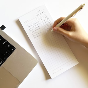 Könnte beinhalten: Ein weißer Notizblock mit einem handschriftlichen Lebensmittelbudget für den Monat Juni. Das Budget umfasst Kategorien wie Lebensmittel einkaufen, Mittagessen auswärts, Abendessen mit Freunden, Supermarkt, mexikanisch, frische Lebensmittel und Salatbar. Das Gesamtbudget beträgt 600 €.