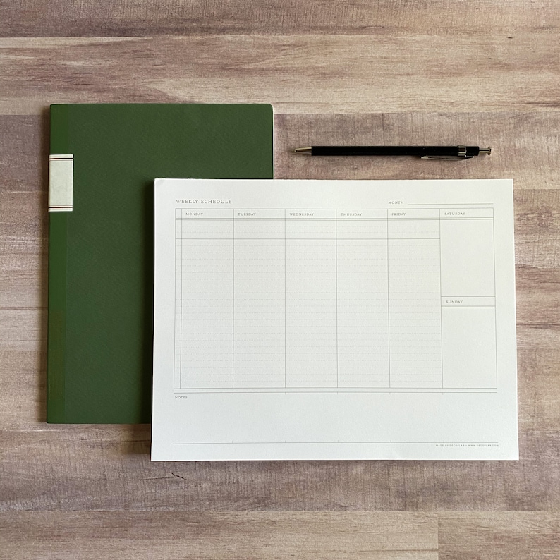 K&ouml;nnte beinhalten: Ein w&ouml;chentlicher Terminplaner mit einem gr&uuml;nen Notizbuch auf einer Holzoberfl&auml;che. Der Planer hat einen Bereich f&uuml;r jeden Tag der Woche mit Platz f&uuml;r Notizen und Termine. Der Planer ist auf wei&szlig;em Papier mit schwarzen Linien gedruckt.