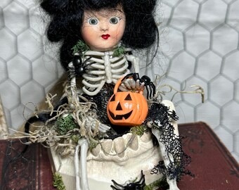 Viñeta de Halloween: Esqueleto alterado con cabeza de muñeca vintage y dientes de yeso. Decoración espeluznante para estante.