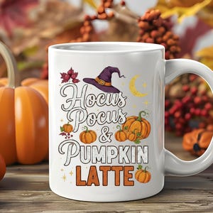 Puede incluir: Taza de cerámica blanca con el texto "Hocus Pocus & Pumpkin Latte", con un sombrero de bruja, calabazas y una luna creciente. La taza tiene un asa grande y está sobre un fondo otoñal con calabazas y follaje.