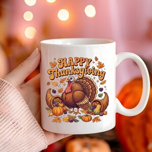 Puede incluir: Taza de cerámica blanca con diseño de Acción de Gracias. La taza muestra el texto "Happy Thanksgiving" en naranja, junto con un pavo, cuernos de la abundancia, calabazas y hojas de otoño. La taza tiene un asa curva.