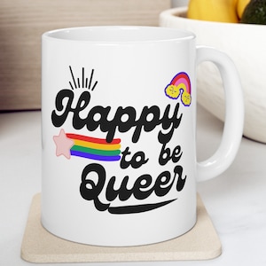 Puede incluir: Taza de cerámica blanca con un diseño de arcoíris y una estrella. La taza tiene texto negro que dice "Happy to be Queer".