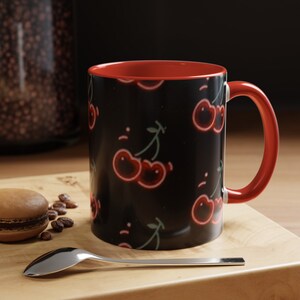 May include: A red and black ceramic mug with a cherry print. The mug has a red handle and a black background with red cherries.