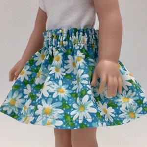 May include: A blue and white floral skirt with a white elastic waistband. The skirt is made of cotton fabric and has a daisy print.