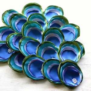 May include: A peacock feather-inspired flower made of blue, green, and purple satin ribbon. The flower is layered and has a three-dimensional effect.