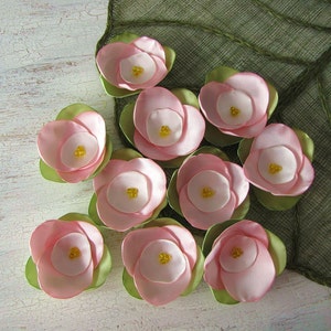 May include: Ten pink fabric flowers with yellow centers, arranged on a green fabric background.