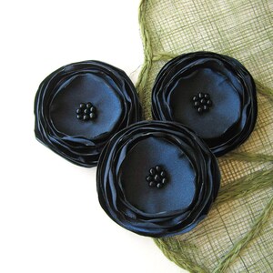 Puede incluir: Tres flores de tela negra con un diseño en capas y centros de cuentas negras.