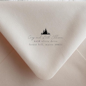 May include: A cream-colored envelope with a black tree design and the text "Cozy and Beth Ellison, 6458 olivia drive, forest hill, maine 49921". The envelope is held by a person.