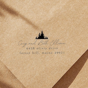 May include: A brown paper envelope with a black tree graphic and the names "Cory and Beth Ellison" printed in a delicate script. The address is also printed in black, including the street address, city, state, and zip code.