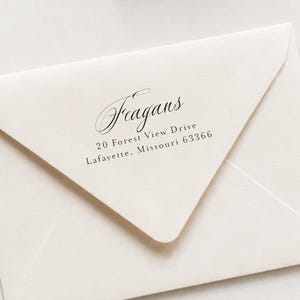 Op de afbeelding: Een zwarte zelfinktende stempel boven een crèmekleurige envelop. De envelop is voorzien van zwarte tekst met de tekst Fragans, 20 Forest View Drive, Lafayette, Missouri 63366 in een combinatie van script- en schreeflettertypes.