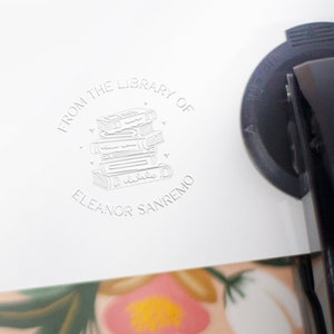 May include: A white rubber stamp with a circular design featuring a stack of books, hearts, and the text "From the Library of Eleanor Sanremo".
