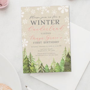 Puede incluir: Una invitaci&oacute;n con tem&aacute;tica invernal con el texto "Please join us for a WINTER Onederland to celebrate Maya Grace's FIRST BIRTHDAY." La invitaci&oacute;n presenta copos de nieve, pinos de acuarela y un fondo beige. Incluye un sobre blanco.