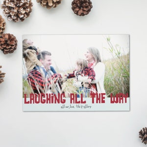 May include: A holiday card featuring a family in a field of tall grass. The family is wearing red and black plaid. The text "LAUGHING ALL THE WAY" is in red, with "all our love, the Kellers" below.