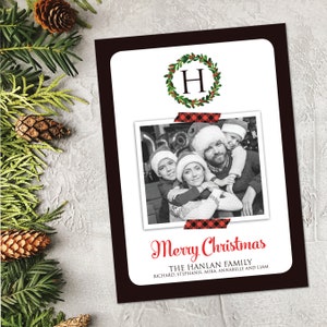 May include: A Christmas card with a family photo, a wreath with the letter "H", and the words "Merry Christmas". The photo is secured with red and black plaid tape. The family's names are listed below the greeting.