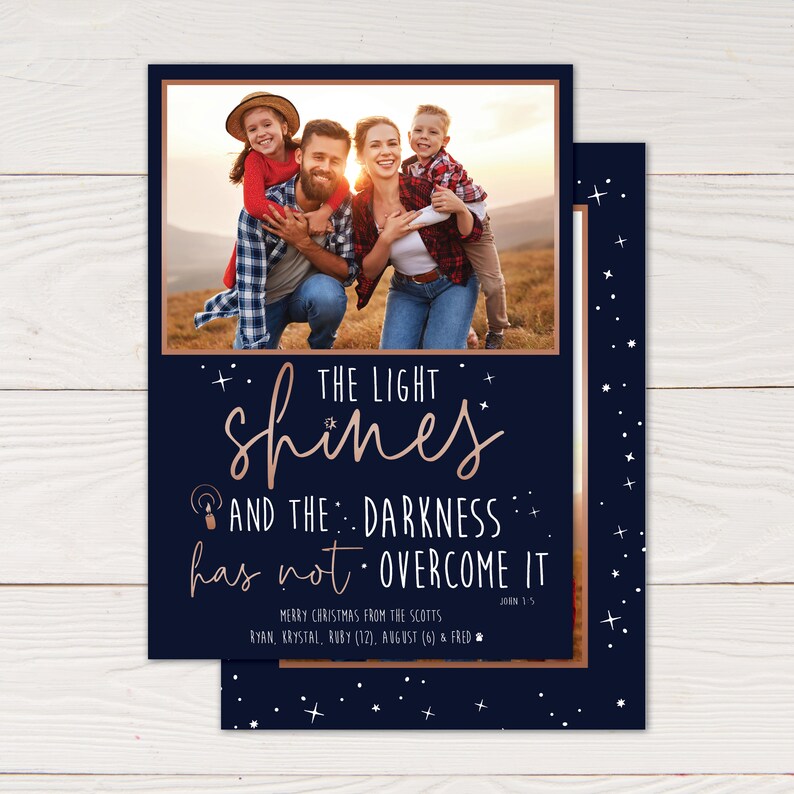 May include: A navy blue Christmas card with a family photo and rose gold text that reads "The light shines and the darkness has not overcome it." The card also includes the family's names and ages.