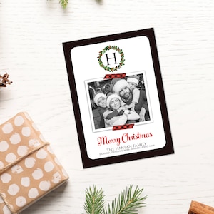 May include: A Christmas card with a black border, featuring a family photo and the words "Merry Christmas." The photo is secured with red and black plaid tape. A green wreath with the letter "H" is at the top.