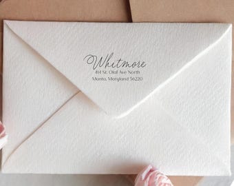 Könnte beinhalten: Ein weißer Umschlag mit dem Namen "Whitmore" in eleganter Schrift gedruckt. Die Adresse lautet "414 St. Olaf Ave North, Manta, Maryland 56220". Der Umschlag ist geschlossen und hat eine strukturierte Oberfläche.