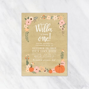 May include: A rectangular invitation card with a kraft paper background. The text "Willa is turning one!" is in white script. Floral and pumpkin illustrations in peach, pink, and green frame the text. Additional text includes event details.