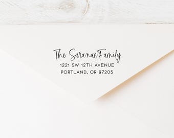 Könnte beinhalten: Cremefarbener Umschlag mit dem Text "The Saranac Family" in Schreibschrift. Darunter steht die Adresse "1221 SW 12TH AVENUE, PORTLAND, OR 97205" in einer einfachen Schriftart. Der Umschlag ist angewinkelt und zeigt eine Ecke.