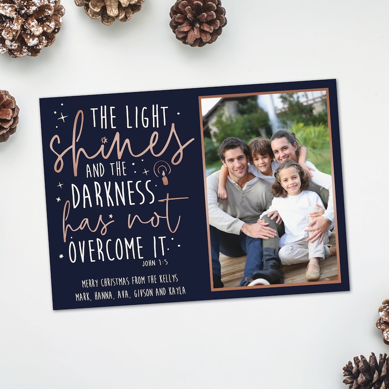 May include: A navy blue Christmas card with a family photo and the text "THE LIGHT shines AND THE DARKNESS has not OVERCOME IT." The card includes the family's names and a Bible verse.