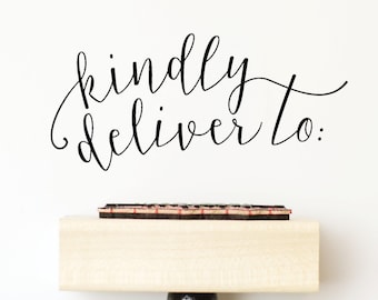 May include: A wooden stamp with the words "kindly deliver to:" in elegant black script. The stamp has a light-colored wooden block and a black handle, set against a white background. The stamp's ink pad is visible.