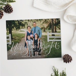 May include: A holiday card with a family portrait and the words "Merry and Bright" in elegant script. The family is standing on a path in front of a white fence and trees. The card includes the text "With Love, The Adams &bull; 2019".