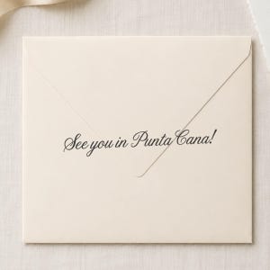 May include: A square cream-colored envelope with a pointed flap. The text "See you in Punta Cana!" is printed in a black, elegant script font across the center of the envelope, positioned just above the bottom edge of the triangular flap.