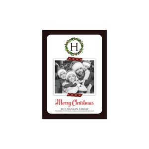 May include: A Christmas card with a black border and a white interior. The card features a family photo, a wreath with the letter "H", and the words "Merry Christmas". The family photo is secured with red and black plaid tape.
