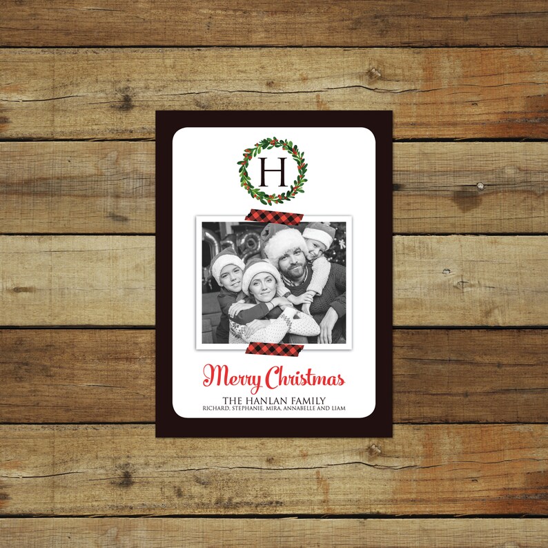 May include: A Christmas card with a family photo, a wreath with the letter "H", and the words "Merry Christmas". The photo is taped to the card with red and black plaid tape. The family is wearing Santa hats.