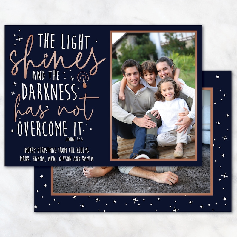 May include: A navy blue Christmas card with a family photo and text that reads "THE LIGHT shines AND THE DARKNESS has not OVERCOME IT." The card has a copper-colored border and star accents. The family photo shows a smiling family of four.