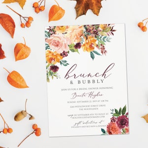 May include: A bridal shower invitation with the words "brunch & bubbly" in a cursive font. The invitation features floral arrangements in shades of orange, peach, and burgundy. The invitation includes details for the event, including the date, time, and location.