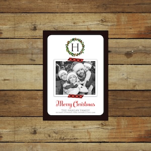 May include: A Christmas card with a family photo, a wreath with the letter "H", and the words "Merry Christmas". The family photo is taped to the card with red and black plaid tape. The card has a dark brown border.