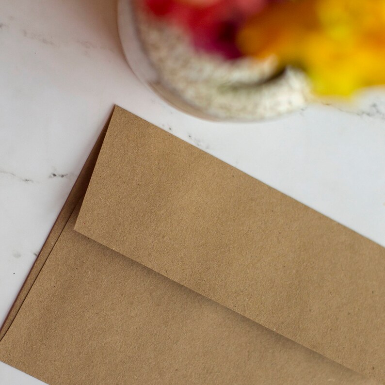 Puede incluir: Dos sobres de papel marr&oacute;n, uno ligeramente superpuesto al otro, est&aacute;n colocados en diagonal. Los sobres tienen una superficie texturizada y est&aacute;n sobre un fondo de m&aacute;rmol blanco. La esquina superior de los sobres es visible.