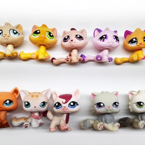 May include: A collection of ten colorful plastic toy cats. The cats are in various poses and have different colored fur, eyes, and noses.