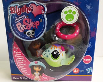 May include: Blythe Littlest Pet Shop Swim & Sun playset featuring a green and blue fish with a pink and white inner tube. The set includes two Blythe dolls with blue and pink hats.