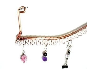 May include: A copper wire earring holder with three pairs of earrings hanging from it. The earrings are made of silver, black, and pink beads.