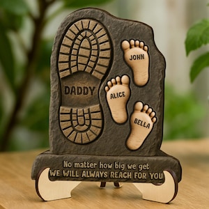 May include: A wooden plaque with a footprint and the words "Daddy", "Alice", "John", and "Bella" engraved on it. The plaque also has the text "No matter how big we get, we will always reach for you".
