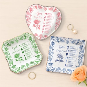 Puede incluir: Tres platos decorativos de cerámica con diseños florales y textos inspiradores. Uno tiene forma de corazón con flores rosas, otro cuadrado con flores azules y el tercero cuadrado con flores verdes. Cada plato tiene un borde dorado.